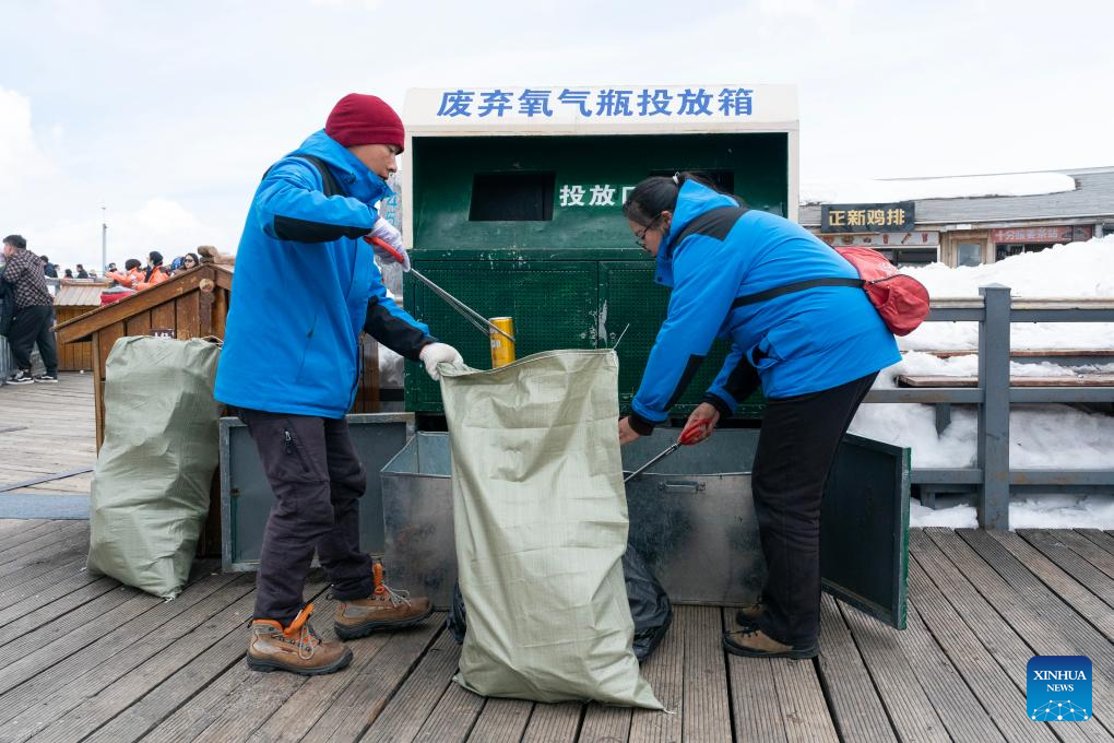 He Dejun (kiri) dan He Xinglan mengumpul silinder oksigen yang tidak digunakan lagi di taman glasier Gunung Sali Yulong  di provinsi Yunnan pada 26 Mac. (Xinhua/Chen Xinbo)